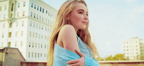 a young woman in a blue sweater is standing on a rooftop .