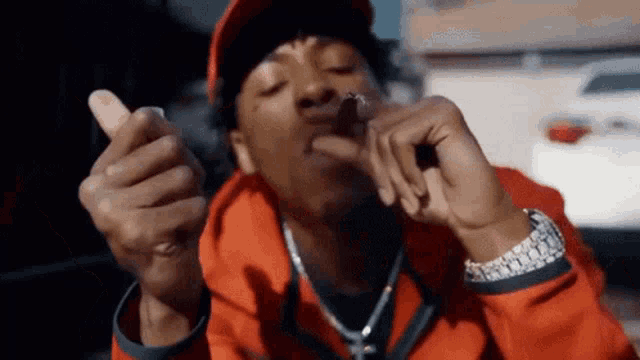 a man in a red jacket and hat is smoking a cigarette and giving a thumbs up .