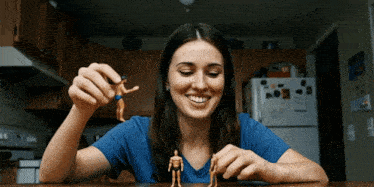 a woman in a blue shirt is smiling while playing with a toy man