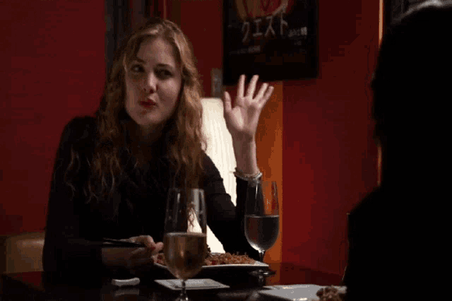 a woman sits at a table with a glass of wine and a plate of food