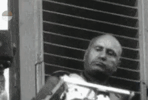 a black and white photo of a man sitting in front of a window holding a gun .