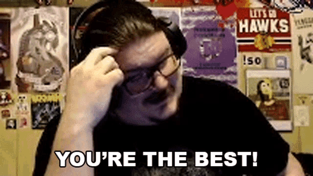 a man wearing headphones and glasses is sitting in front of a wall with posters and says `` you 're the best ''