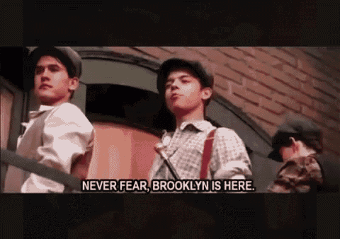 a group of young men are standing in front of a brick building and one of them is saying " never fear brooklyn is here "