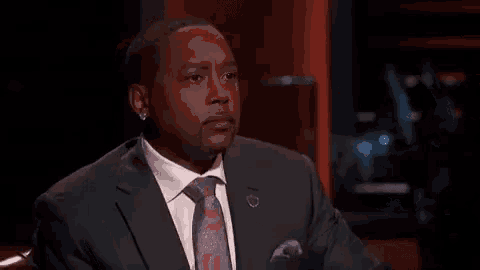 a man in a suit and tie is sitting in a dark room .