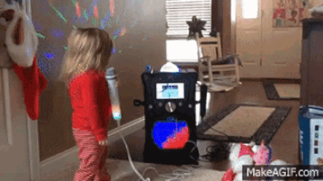 a little girl is singing into a microphone in front of a makeagif.com sign