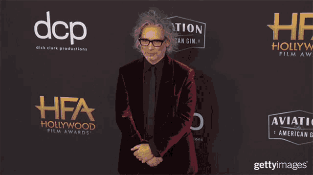 a man in a red suit stands in front of a hollywood film awards logo