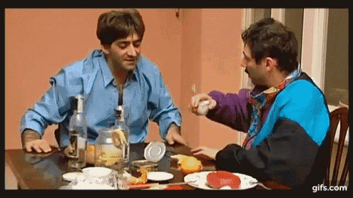 two men are sitting at a table eating food and drinking alcohol ..