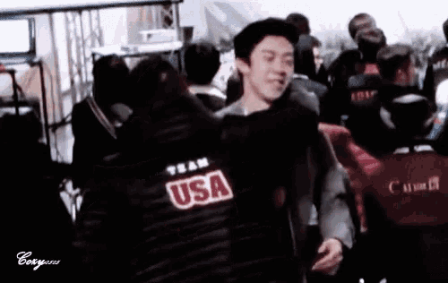 a man wearing a black usa jacket stands in a crowd of people