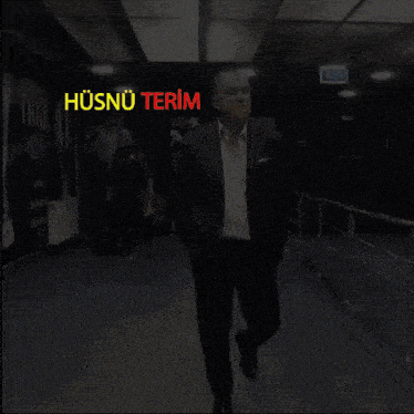 a man in a suit walks down a hallway with a sign that says husnu terim on it