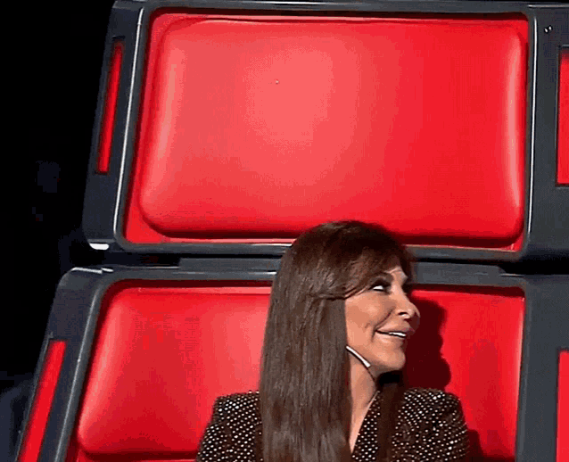 a woman with long hair is sitting in a red chair and smiling .