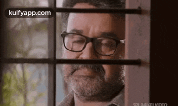 a man with glasses is looking out of a window .