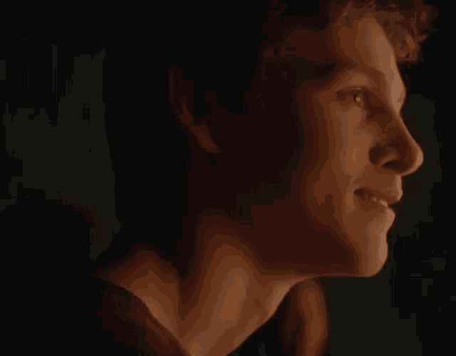 a close up of a young man 's face in a dark room with a green background .