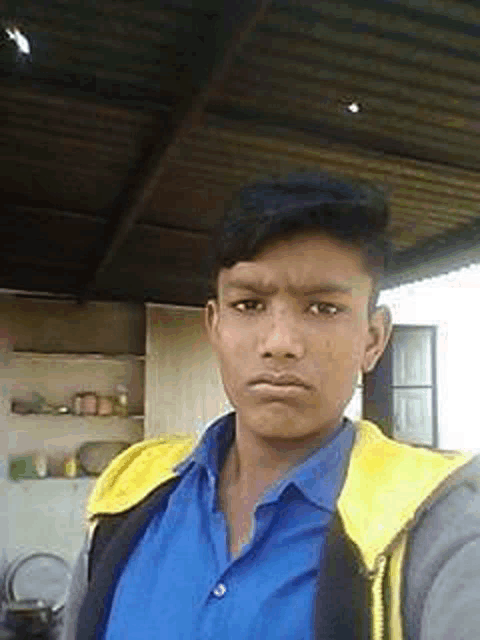 a young man wearing a blue shirt and a yellow jacket is standing under a roof .