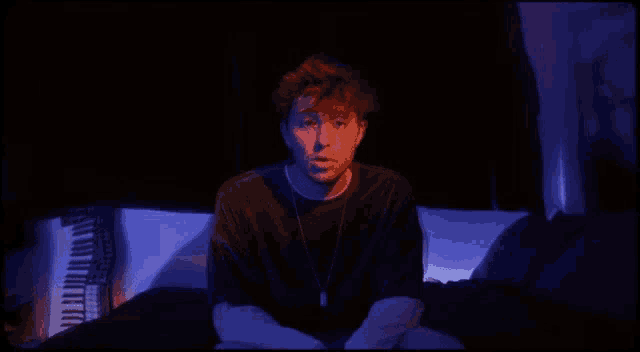 a man is sitting on a bed in a dark room with a piano in the background .