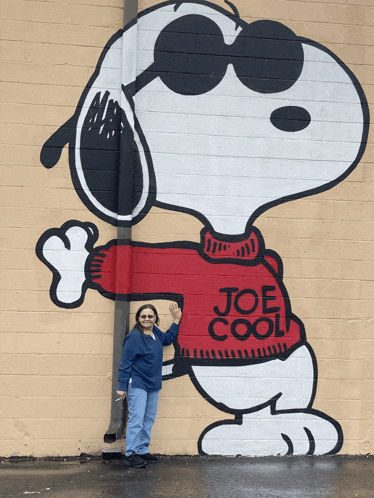 a woman is standing in front of a snoopy mural that says joe cool