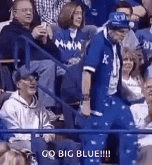 a group of people are sitting in a stadium watching a game and a man is standing in the middle of the crowd .