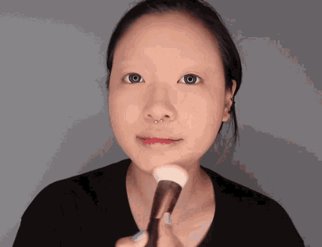 a woman applying makeup with a brush on her face