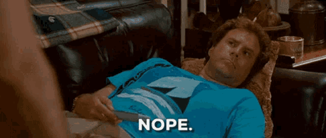 a man in a blue shirt is laying on a couch with the word nope in front of him