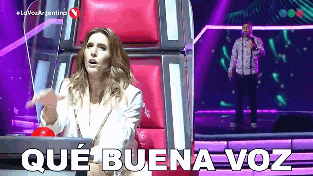 a woman sitting in a chair next to a man singing and the words que buena voz written on the screen