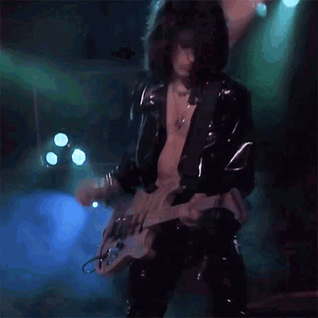 a man in a leather jacket is playing a guitar