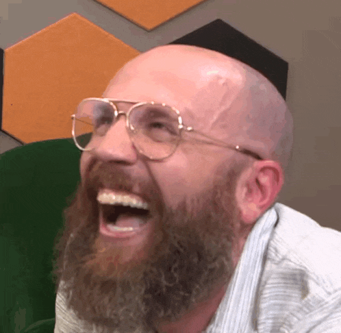 a bald man with a beard and glasses is laughing with his mouth open