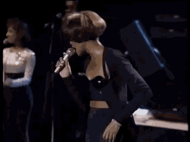 a woman in a black crop top is singing into a microphone .