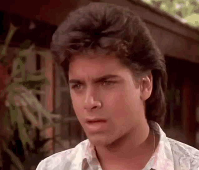 a young man with a mullet is standing in front of a house and making a funny face .