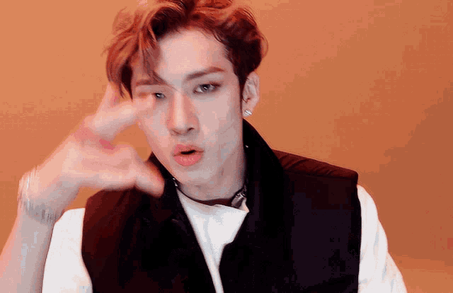 a young man wearing a black vest and a white shirt is making a gesture with his hand