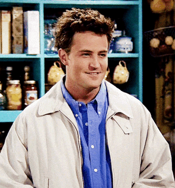 a man wearing a white jacket and a blue shirt smiles
