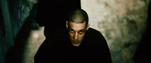 a man with a shaved head is wearing a black shirt and looking at the camera .