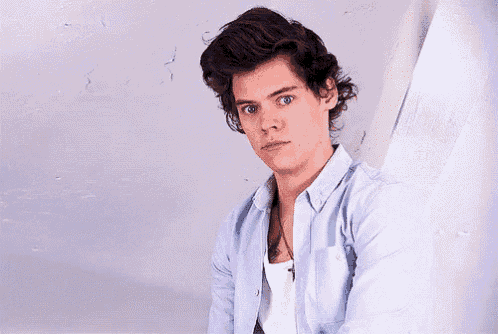 harry styles is making a funny face while wearing a light blue shirt .