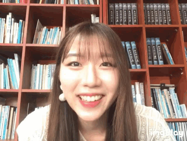 a woman is smiling in front of a bookshelf filled with books including one that says ' a ' on it