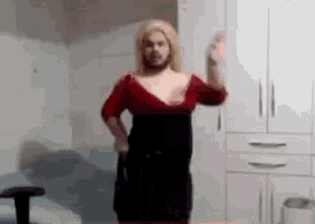 a man with a beard is dancing in a room while wearing a red dress .