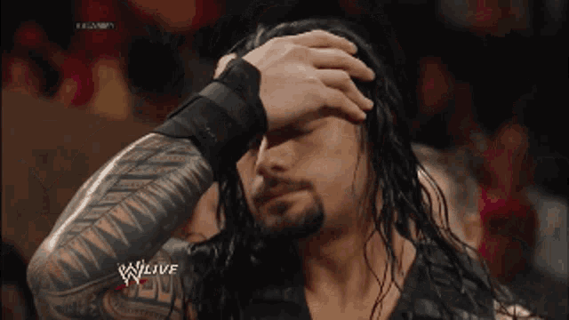 a man with a tattoo on his arm holds his hand to his forehead in front of a screen that says wwe live