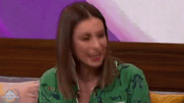 a woman in a green shirt is sitting on a couch laughing .