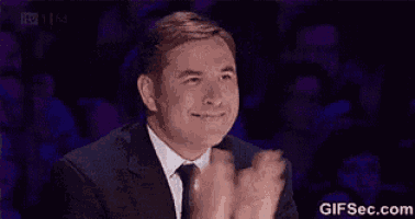 a man in a suit and tie is applauding while sitting in front of a crowd .