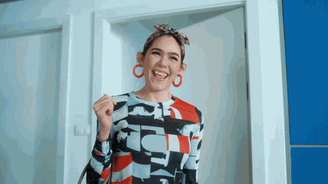 a woman wearing a colorful shirt and red earrings is smiling