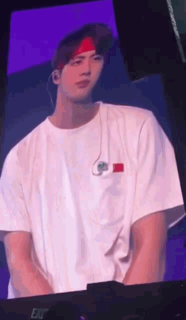 a man wearing a white shirt and a red headband is sitting on a stage