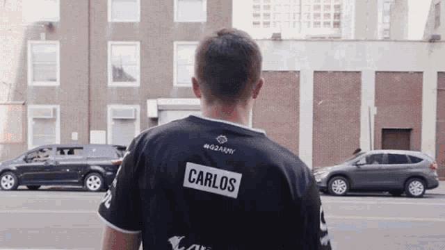 a man wearing a shirt that says carlos is walking down the street