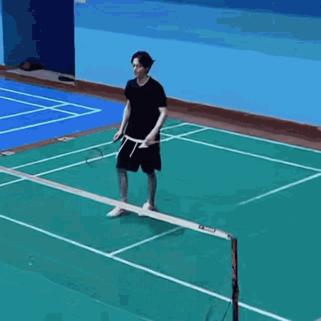 a man in a black shirt is playing badminton on a court .