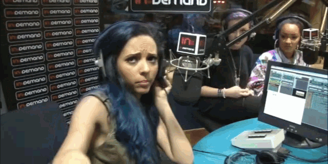 a woman with blue hair talks into a microphone in front of a sign that says " demand "