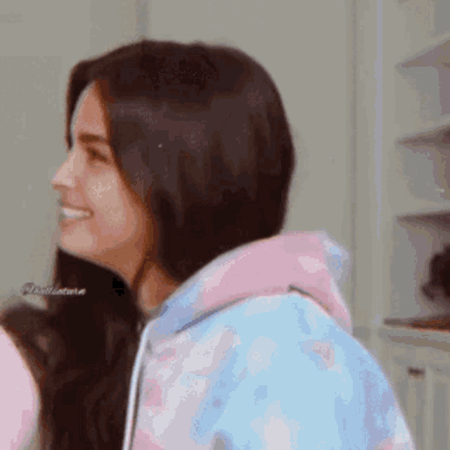 a woman wearing a pink and blue hoodie is smiling and looking to the side .
