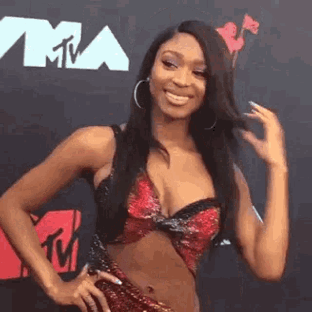 a woman in a crop top and hoop earrings is smiling on a red carpet .