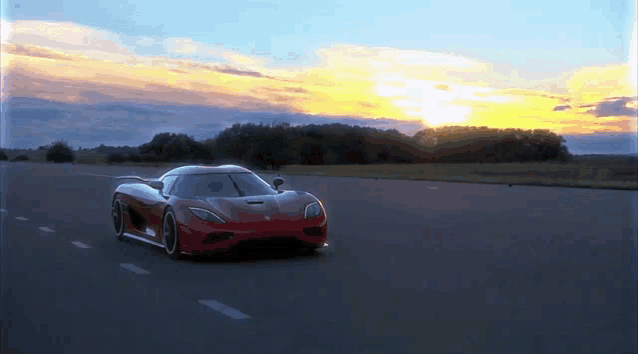 a red sports car is driving down a road with the sun setting in the background