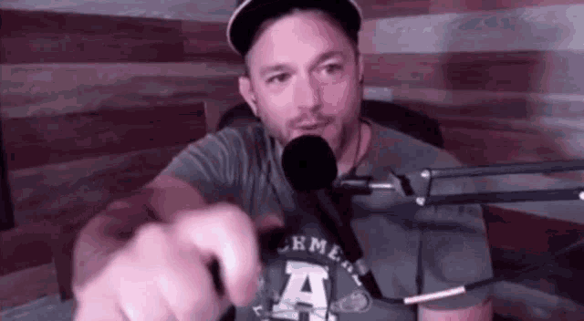 a man wearing a hat and a t-shirt with the letter a on it is sitting in front of a microphone .