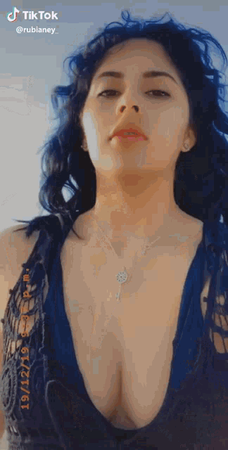 a woman wearing a blue top and a necklace with a key on it is looking at the camera .