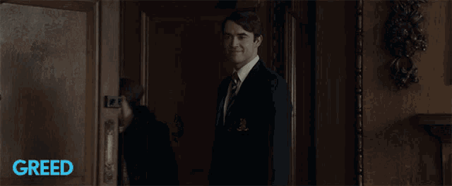 a man in a suit and tie opens a door with greed written on the bottom