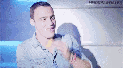 a young man in a denim shirt is smiling and holding a bottle of water .