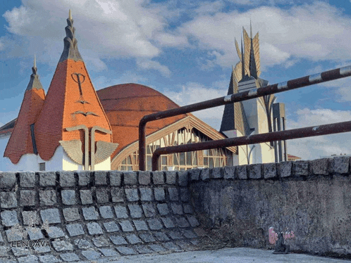 a building with a red roof is behind a stone wall with lenjava written on the bottom