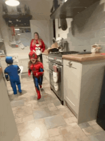 two children in spiderman costumes running in a kitchen